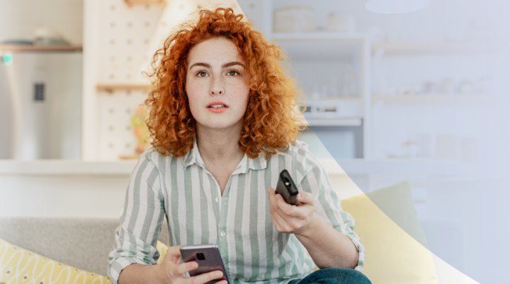 A women holding both her phone and tv remote 